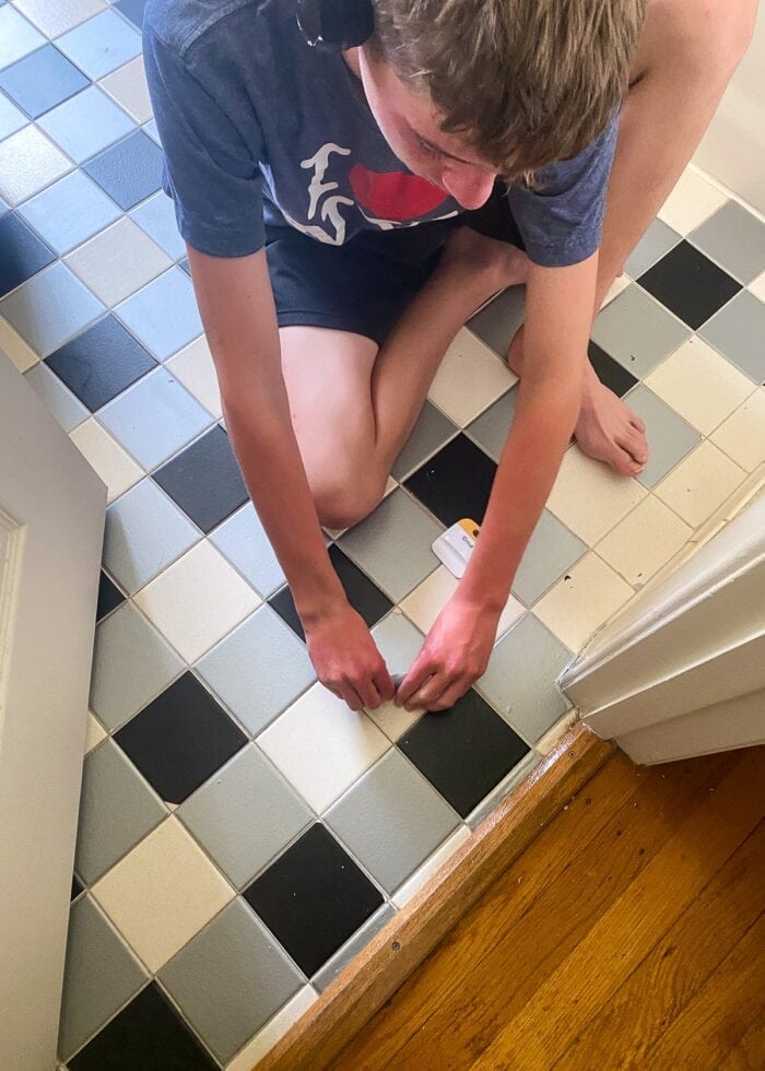 Teenage boy peeling tile stickers off of bathroom floor