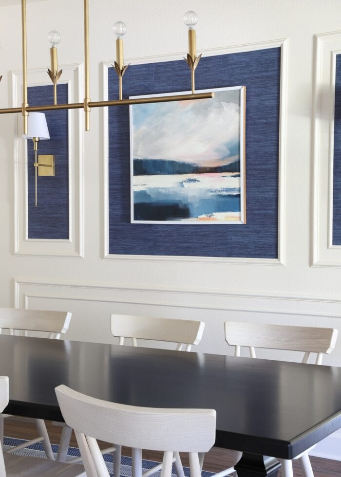 An ivory dining room with a moulding trim wall feature, blue grasscloth wallpaper, and gold light fixtures