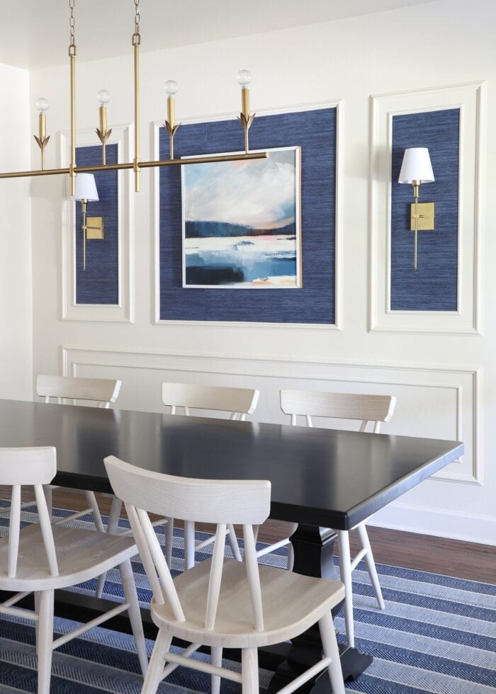 An ivory dining room with a moulding trim wall feature, blue grasscloth wallpaper, and gold light fixtures