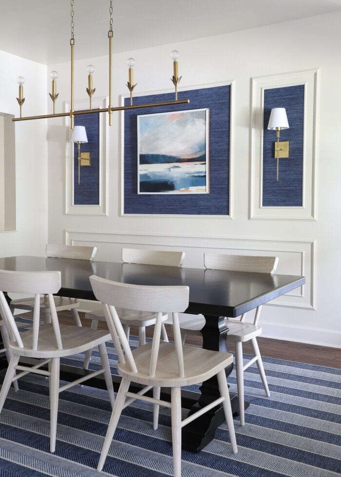 An ivory dining room with a moulding trim wall feature, blue grasscloth wallpaper, and gold light fixtures