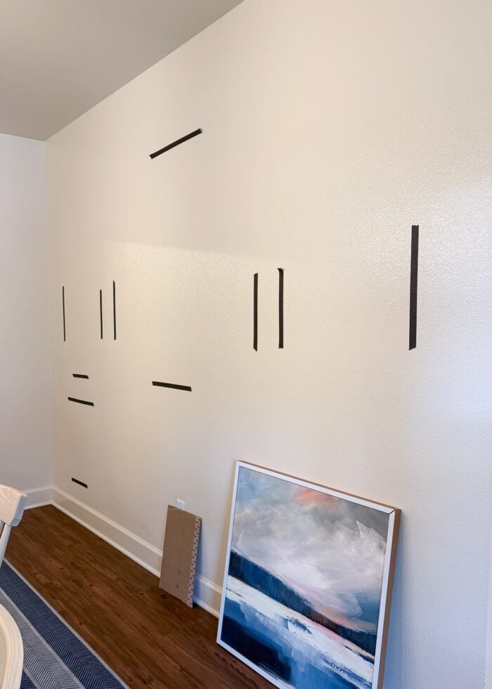 A large empty wall with pieces of tape on it and artwork leaning against the wall