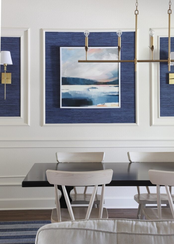 An ivory dining room with a moulding trim wall feature, blue grasscloth wallpaper, and gold light fixtures