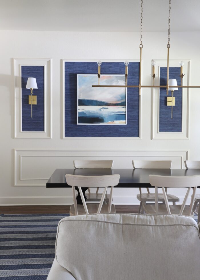 An ivory dining room with a moulding trim wall feature, blue grasscloth wallpaper, and gold light fixtures