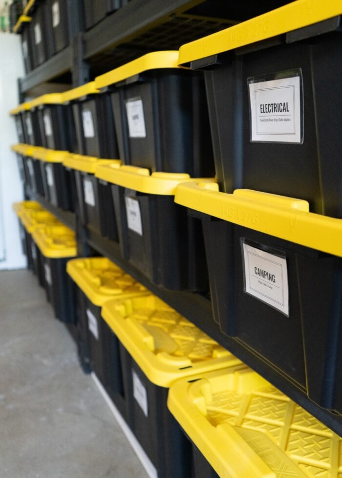Black shelves in a garage filled with different sizes of black and yellow HDX bins with bright white labels on the front.