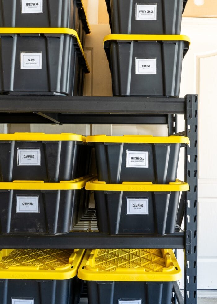 Various sizes of black and yellow HDX bins on a black metal shelf in a garage.