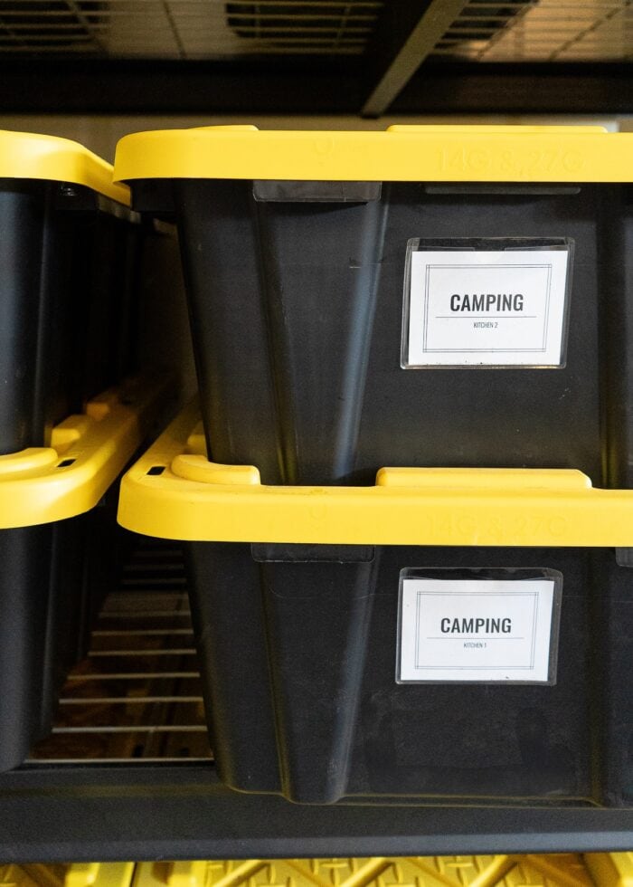 A close up shot of two black and yellow HDX bins with bright white labels holding camping gear