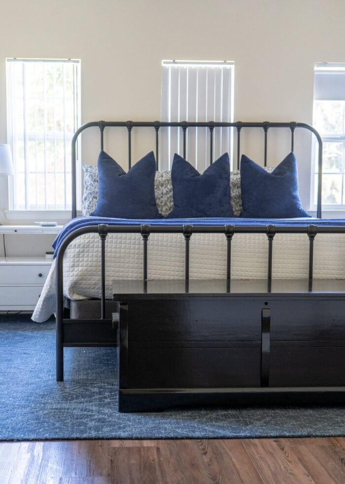 A master bedroom with an iron bed and a painted black cedar chest positioned at the end.