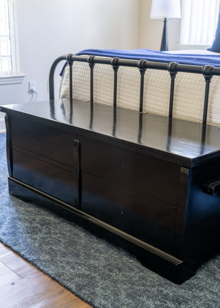 A glossy black painted cedar chest sitting at the foot of a bed.