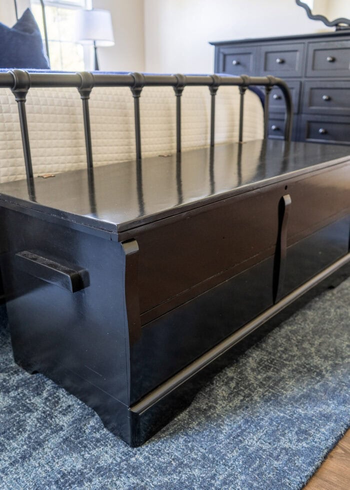A glossy black painted cedar chest sitting at the foot of a bed.