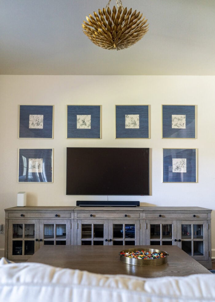 Gallery wall frames hung around a TV filled with scraps of vintage wallpaper as artwork all above a long media cabinet