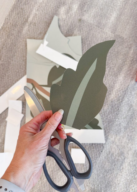 A hand holding a green leaf cut out of a wallpaper mural scrap