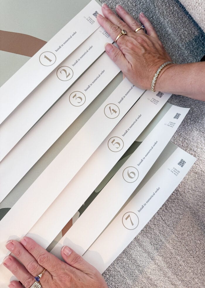Hands holding down sheets panels of a mural to show the panel numbers