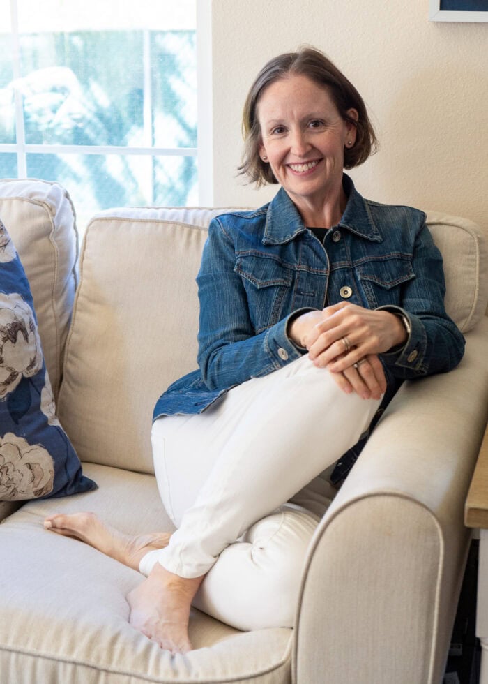 Megan in a jean jacket sitting on a white couch.