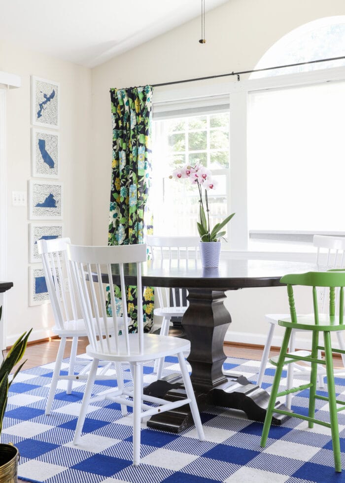 A dark dining room table with white dining chairs on top of a blue and white checked rug