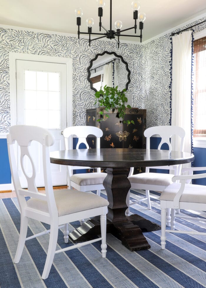 A dark dining room table with painted white chairs on a blue striped rug.