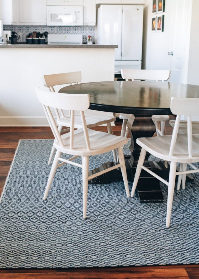 Natural wood chairs around a dark wood dining table on a blue patterned rug.