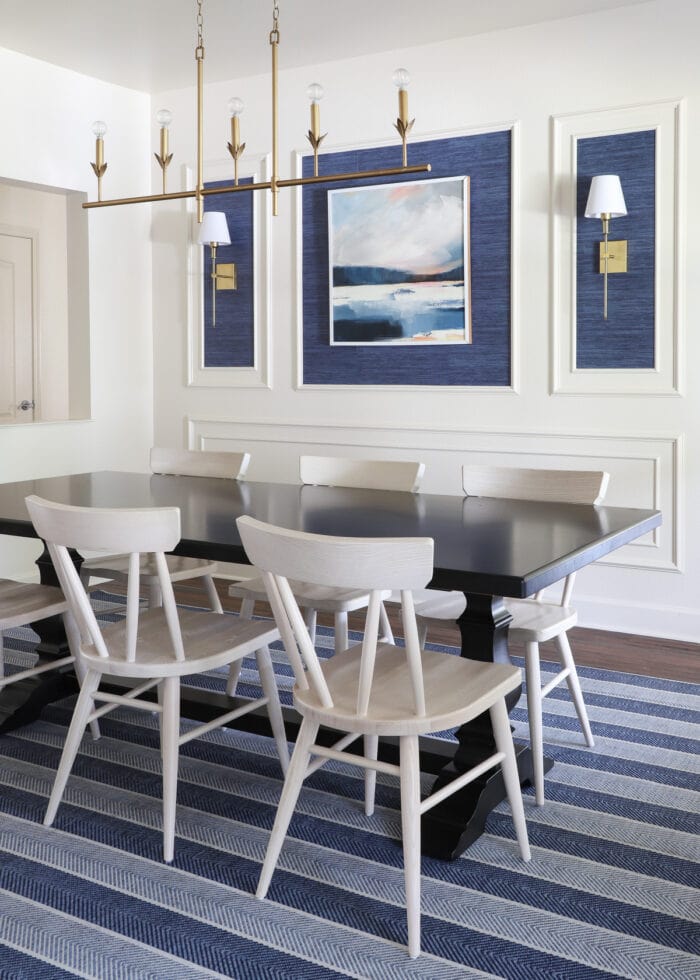 A dark wood dining table with light colored wood dining chairs on a blue striped rug.
