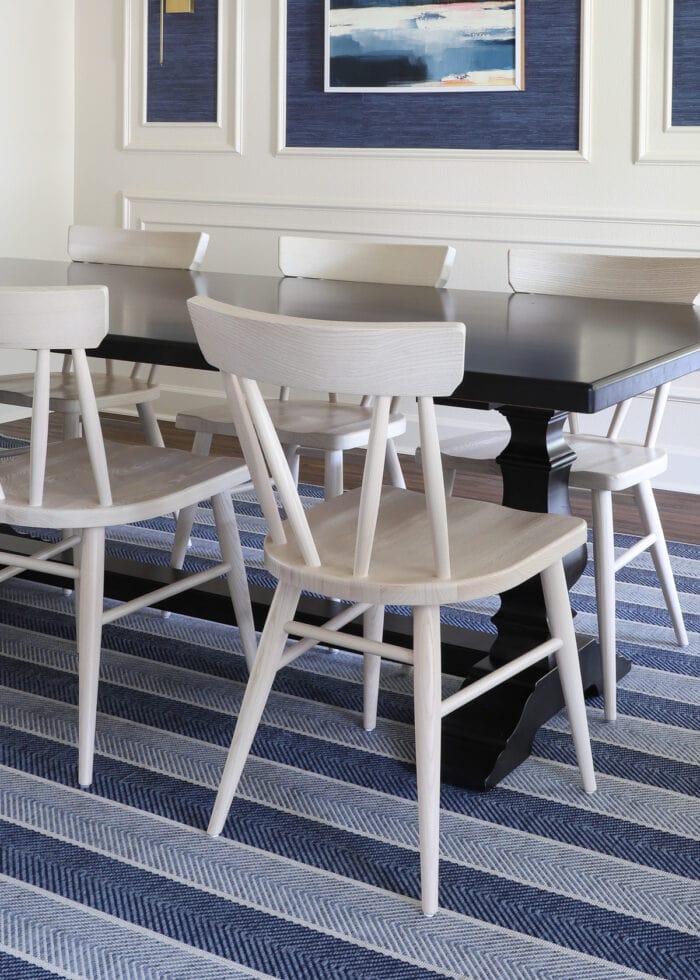 A dark wood dining table with light colored wood dining chairs on a blue striped rug.
