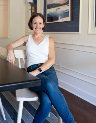 Megan sitting on a light dining room chair next to a dark wood table.