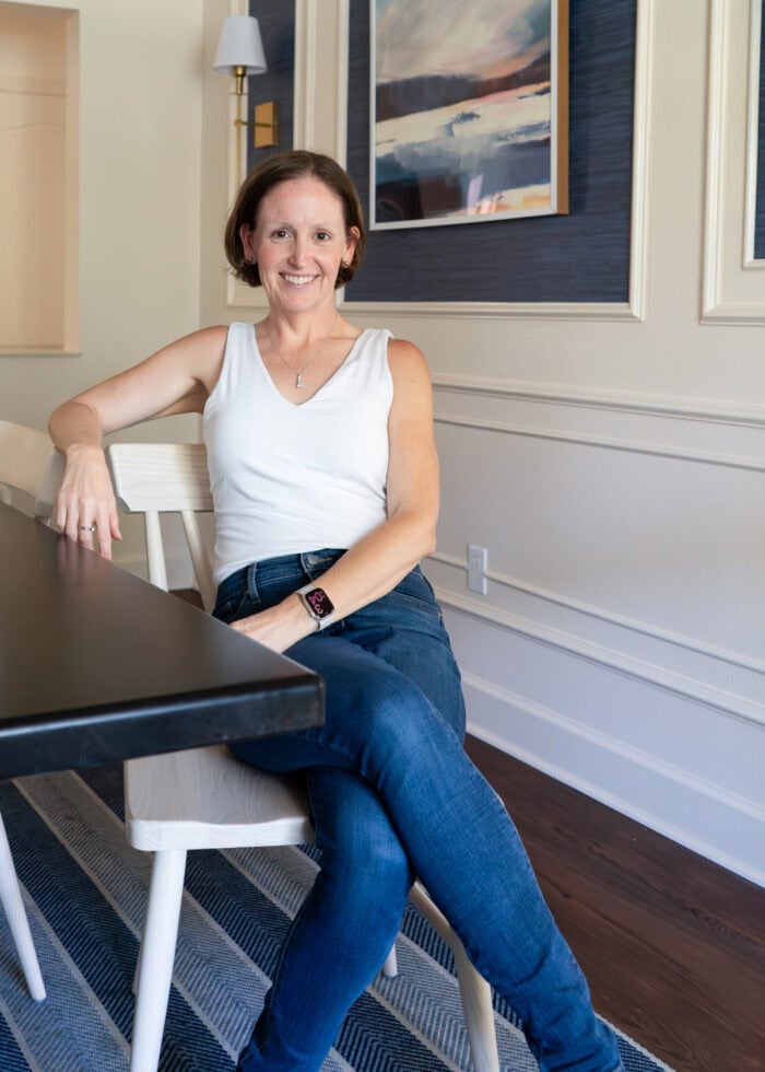Megan sitting on a light dining room chair next to a dark wood table.