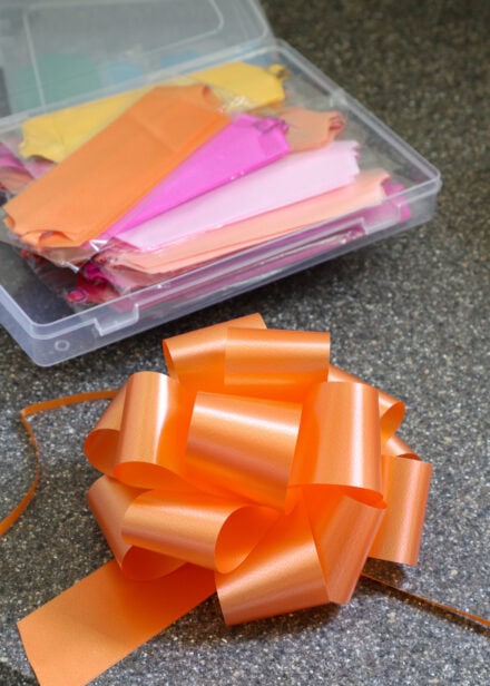 An orange pull bow sitting on a counter next to a box of unpackaged bows