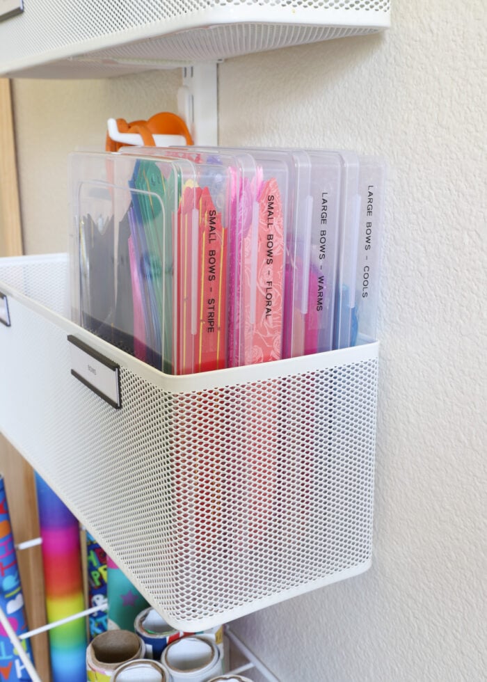 Four plastic cases filled with an assortment of flat pull bows tucked into an Elfa basket