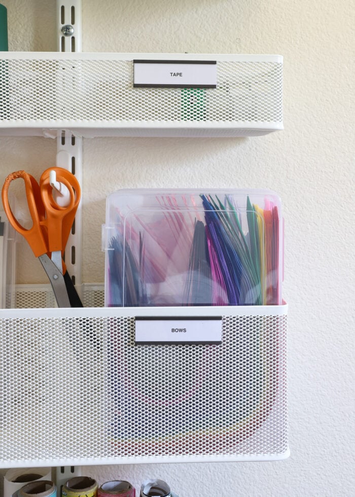 A set of plastic cases holding bows tucked into a large basket on an Elfa storage system mounted to the wall