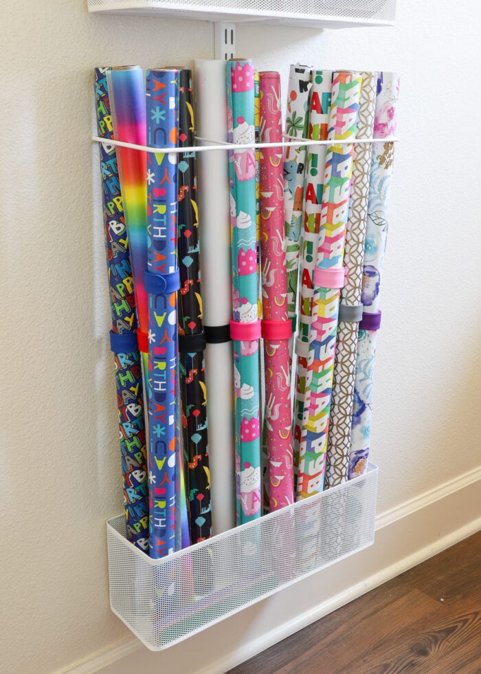Rolls of wrapping paper tucked into a basket and wrapping paper holder on an Elfa storage system mounted to the wall