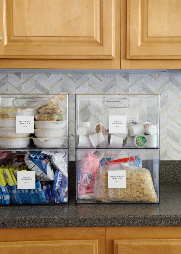Four clear containers sitting on a kitchen counter holding pantry backstock