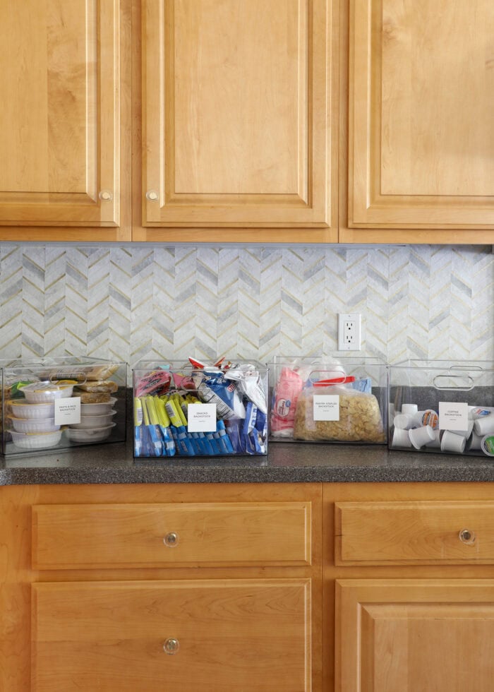 Four clear containers sitting on a kitchen counter holding pantry backstock
