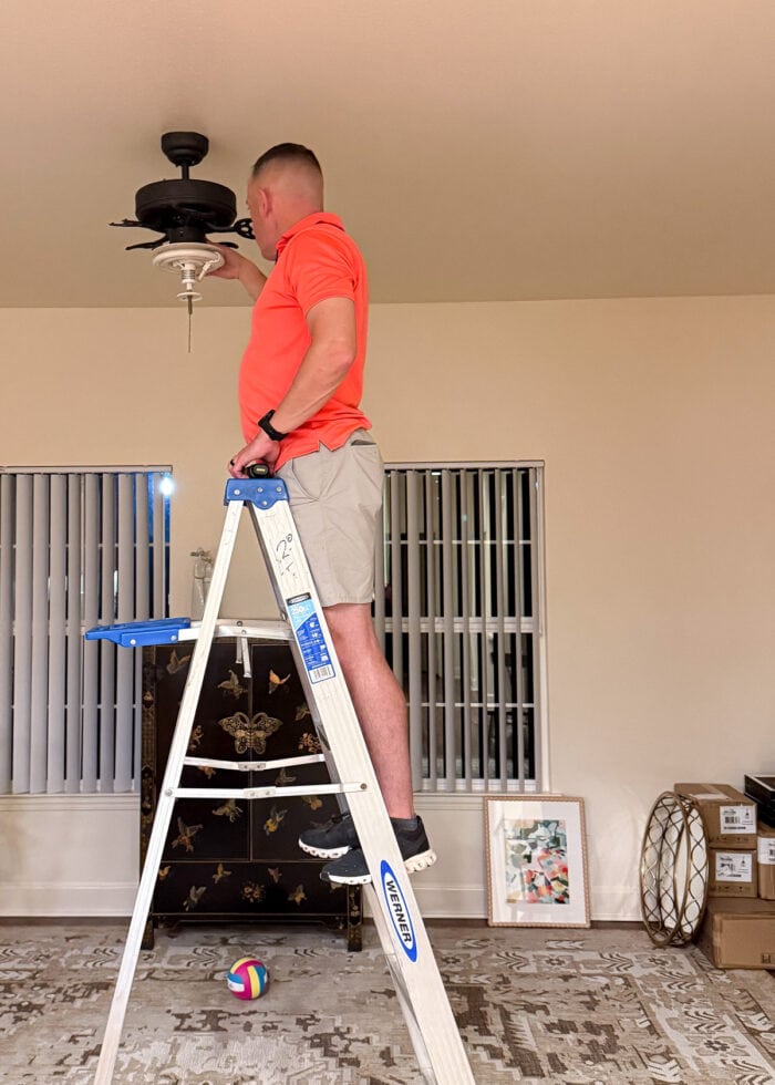 A man on a ladder taking down a ceiling fan.