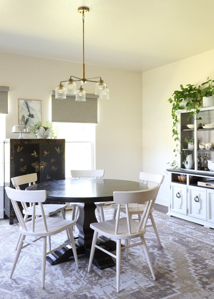 A beige, black, and white dining room with a gold light fixture hung over the table.